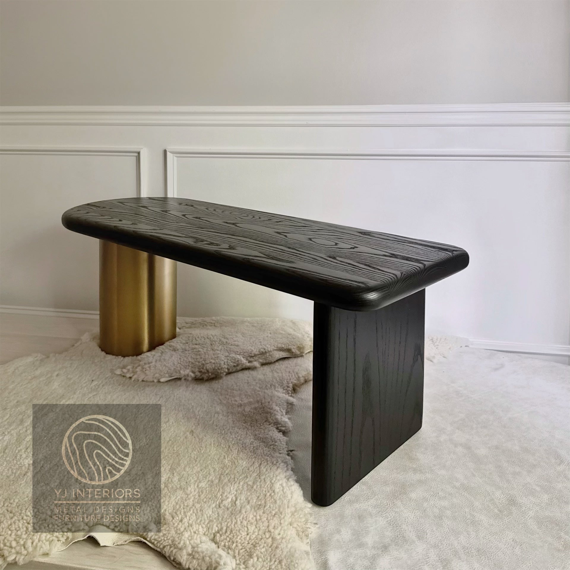 Modern black coffee table bench with gold cylindrical leg against a neutral wall.