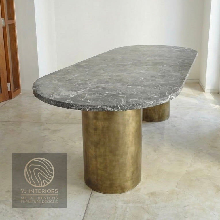 Close-up of the brushed antique brass finish on a round metal table leg. The texture shows a soft, muted gold luster with a vintage patina, highlighting the high-quality metalwork.