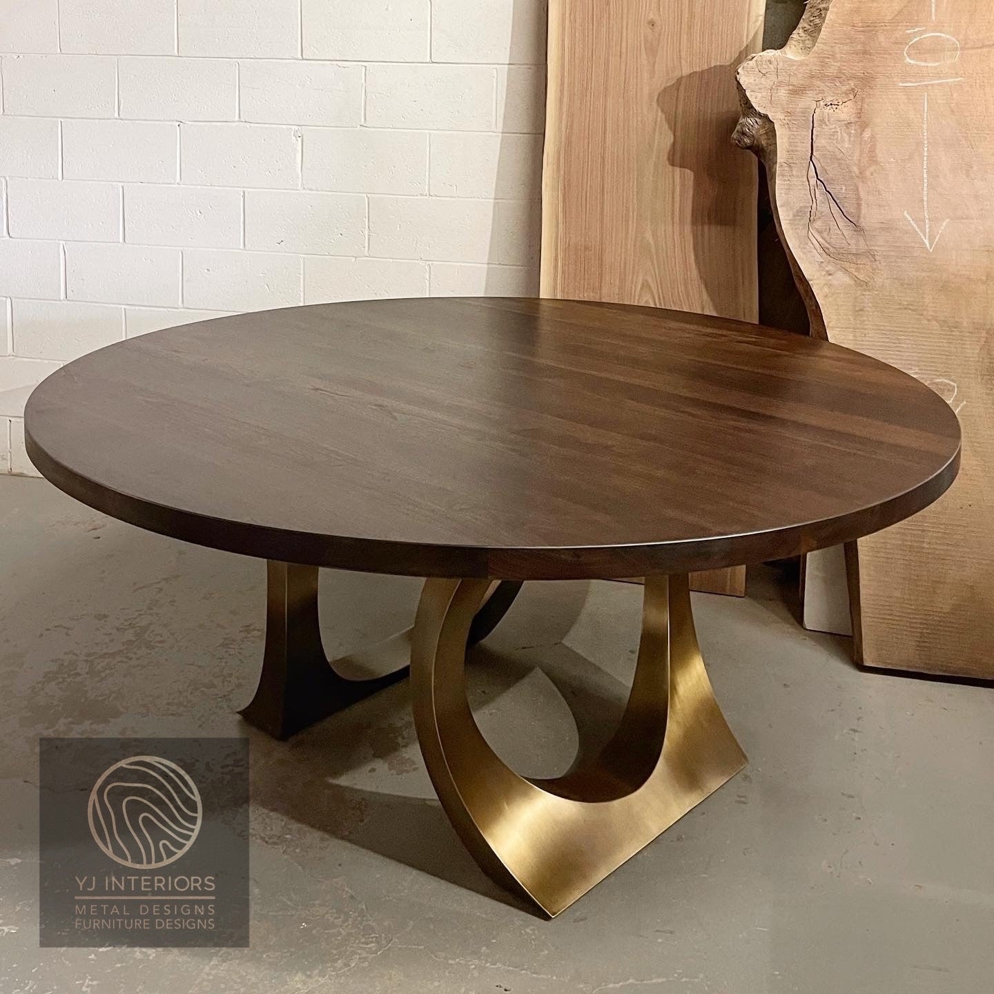 Wooden table with gold metal legs on a gray floor, branded 'YJ Interiors'.