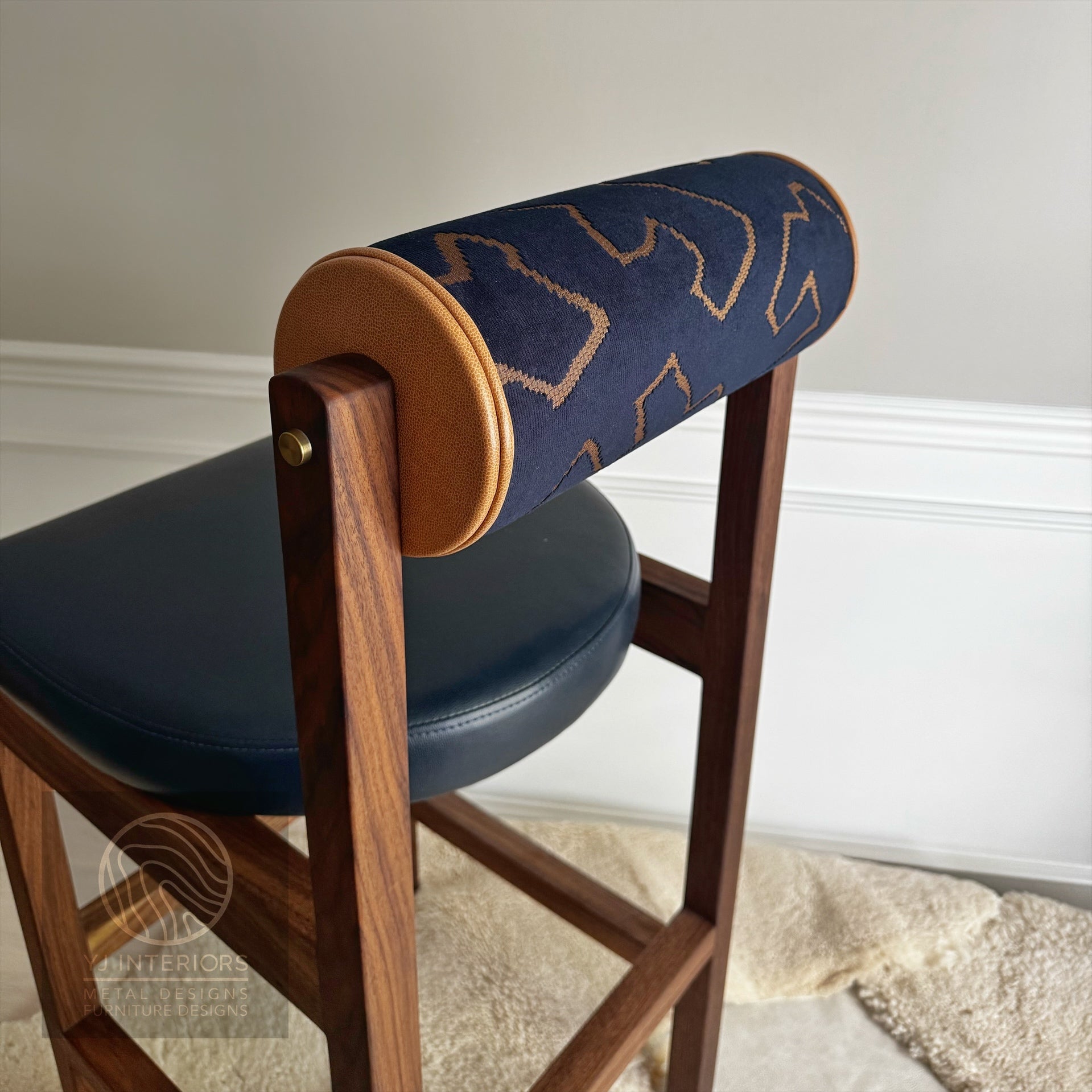 Wooden chair with blue cushioned seat and backrest against a neutral wall.