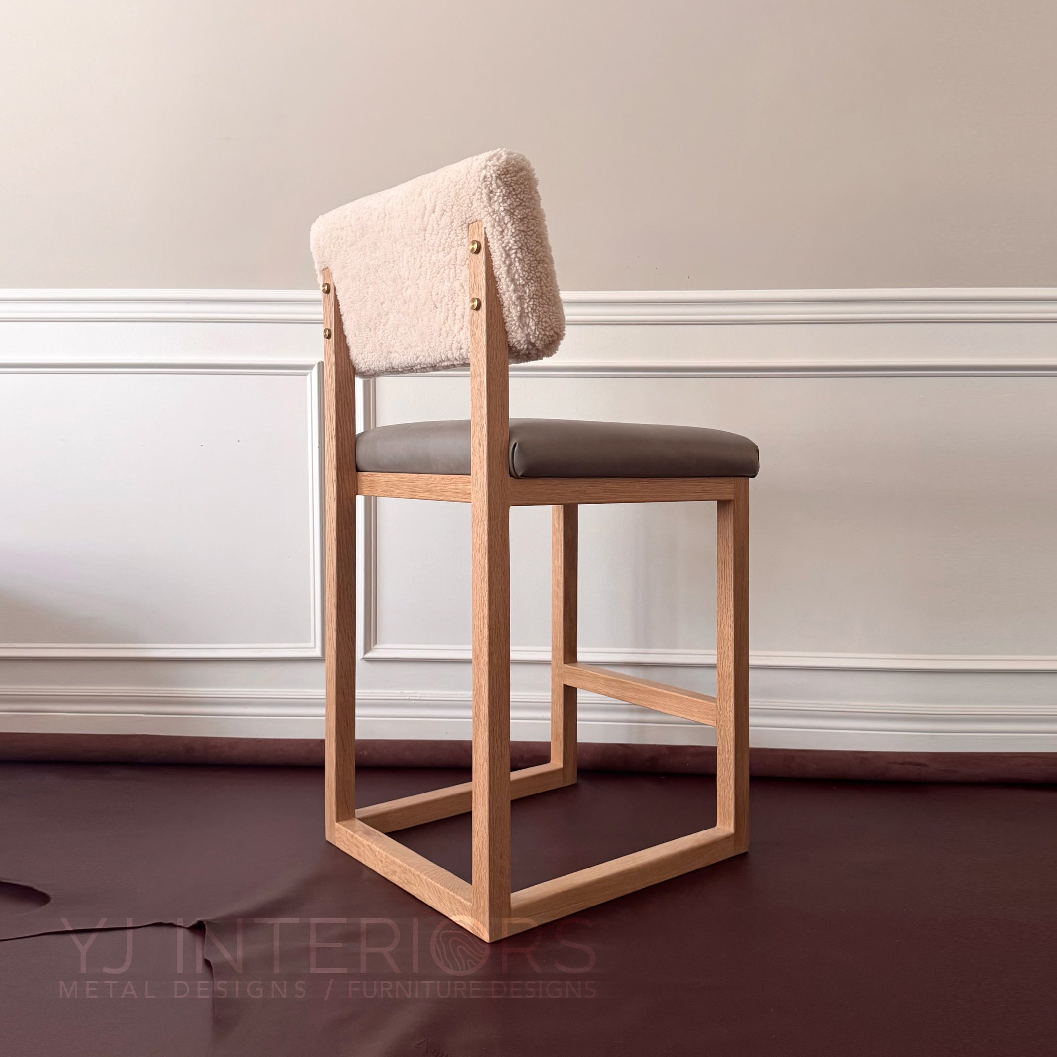 A modern wooden bar stool with a square frame, light natural wood legs, a dark gray upholstered seat, and a textured cream bouclé backrest, set against a neutral interior wall.