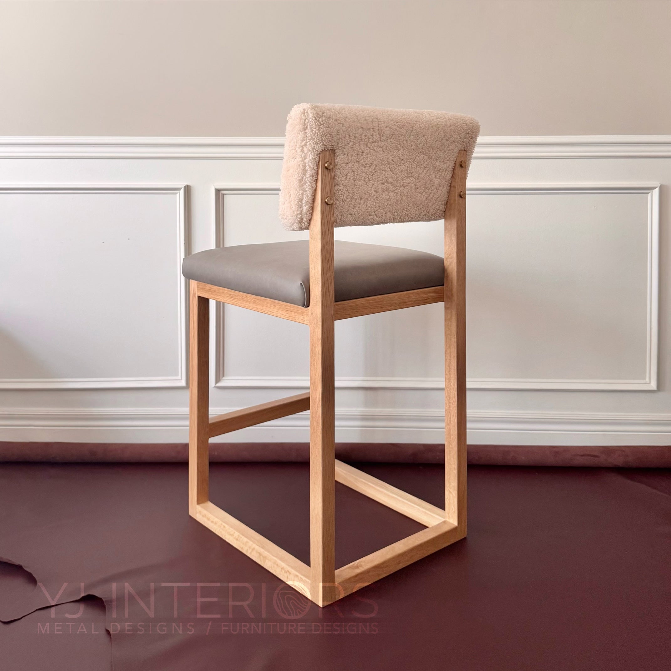 A modern wooden bar stool with a square frame, a light natural wood finish, a gray upholstered seat cushion, and a textured beige bouclé backrest, set against a neutral paneled wall.