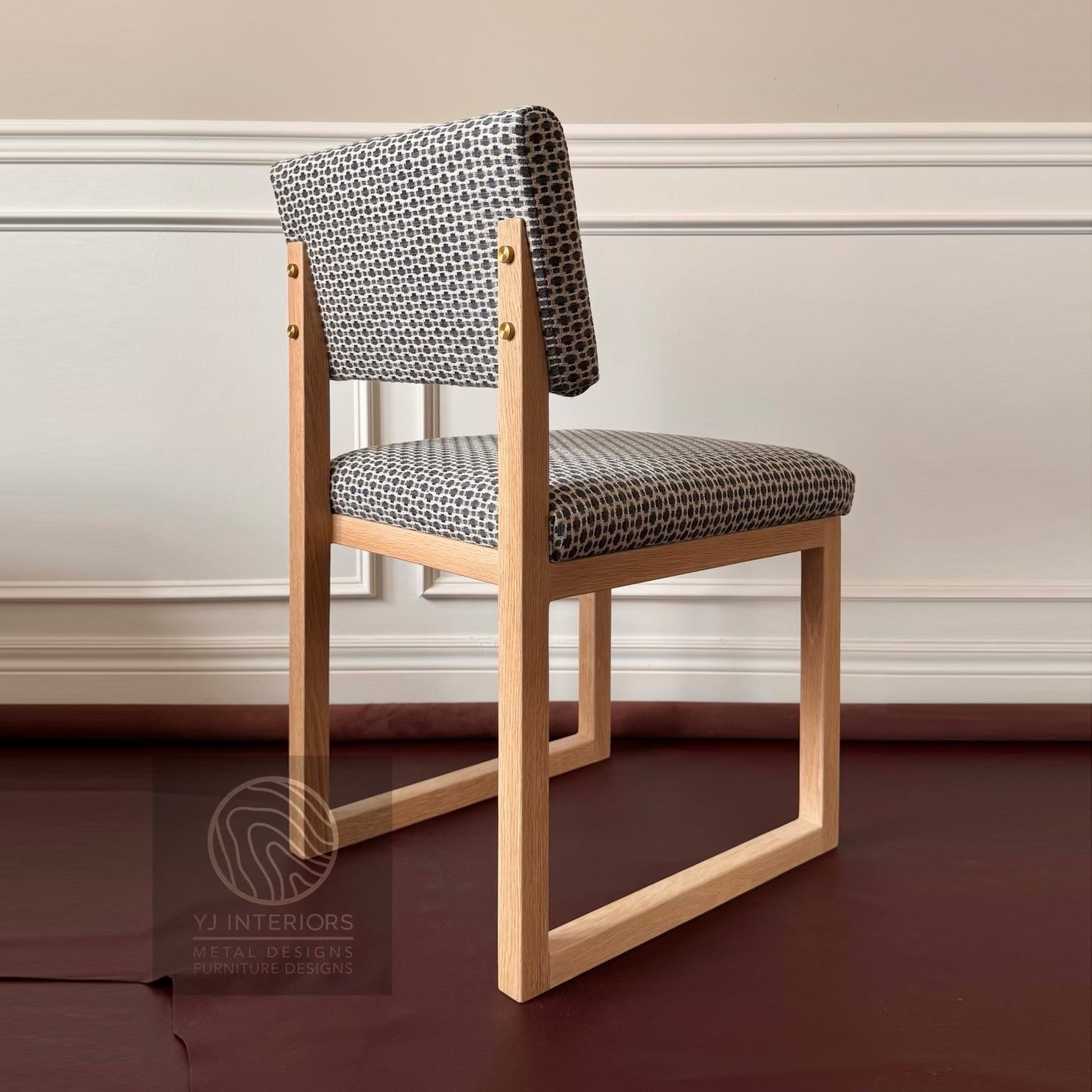 A modern wooden dining chair with a geometric black and white patterned fabric upholstery, shown in a room setting with a dark wood floor and white paneled wall. sq upholstered dining chair