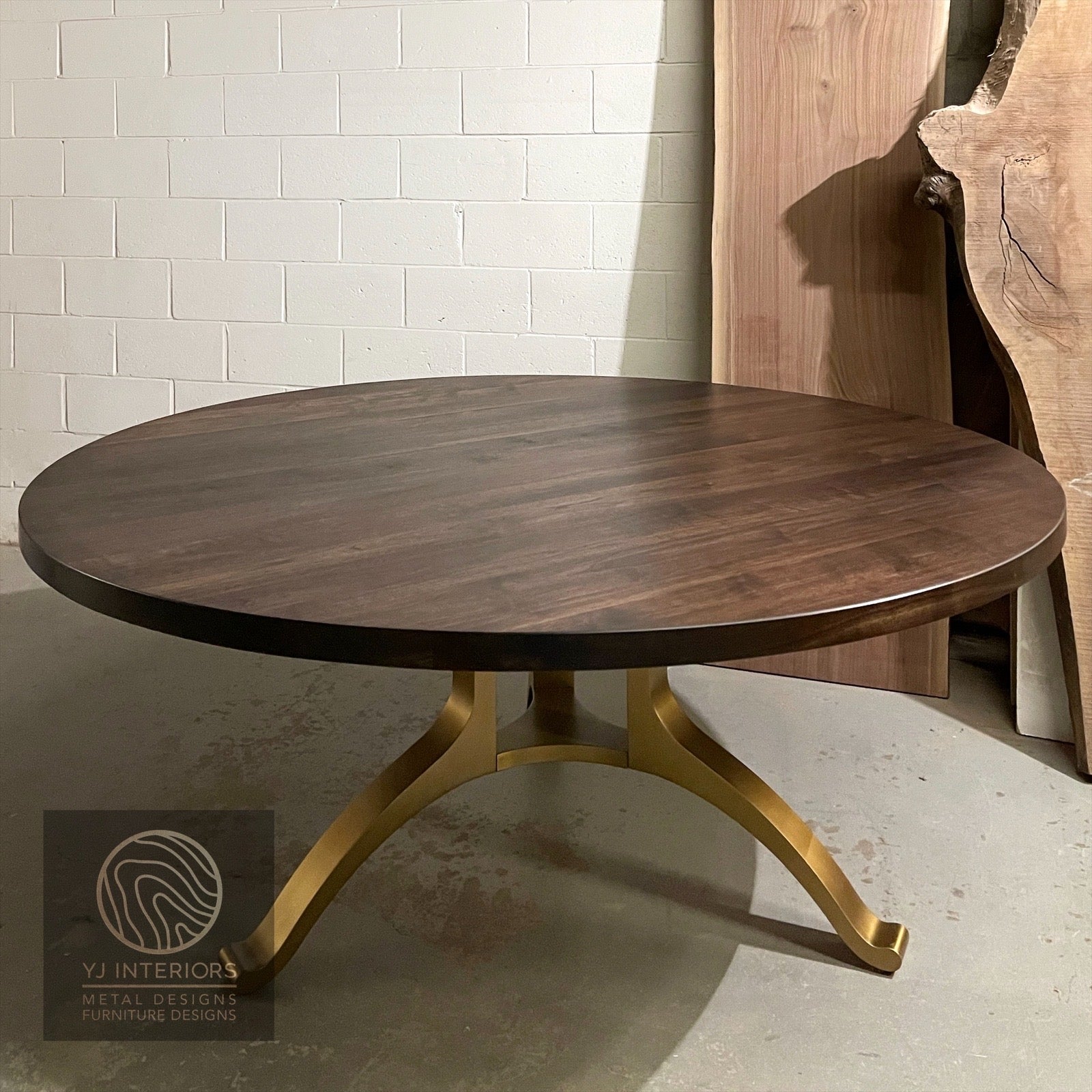 Round wooden table with gold metal legs against a white brick wall.