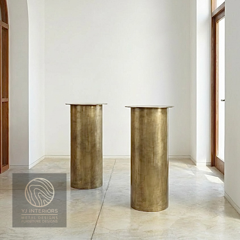 Close-up of the brushed antique brass finish on a round metal table leg. The texture shows a soft, muted gold luster with a vintage patina, highlighting the high-quality metalwork.