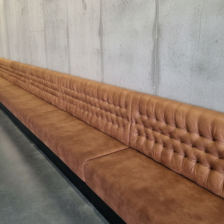 Brown tufted sofa against a concrete wall.
