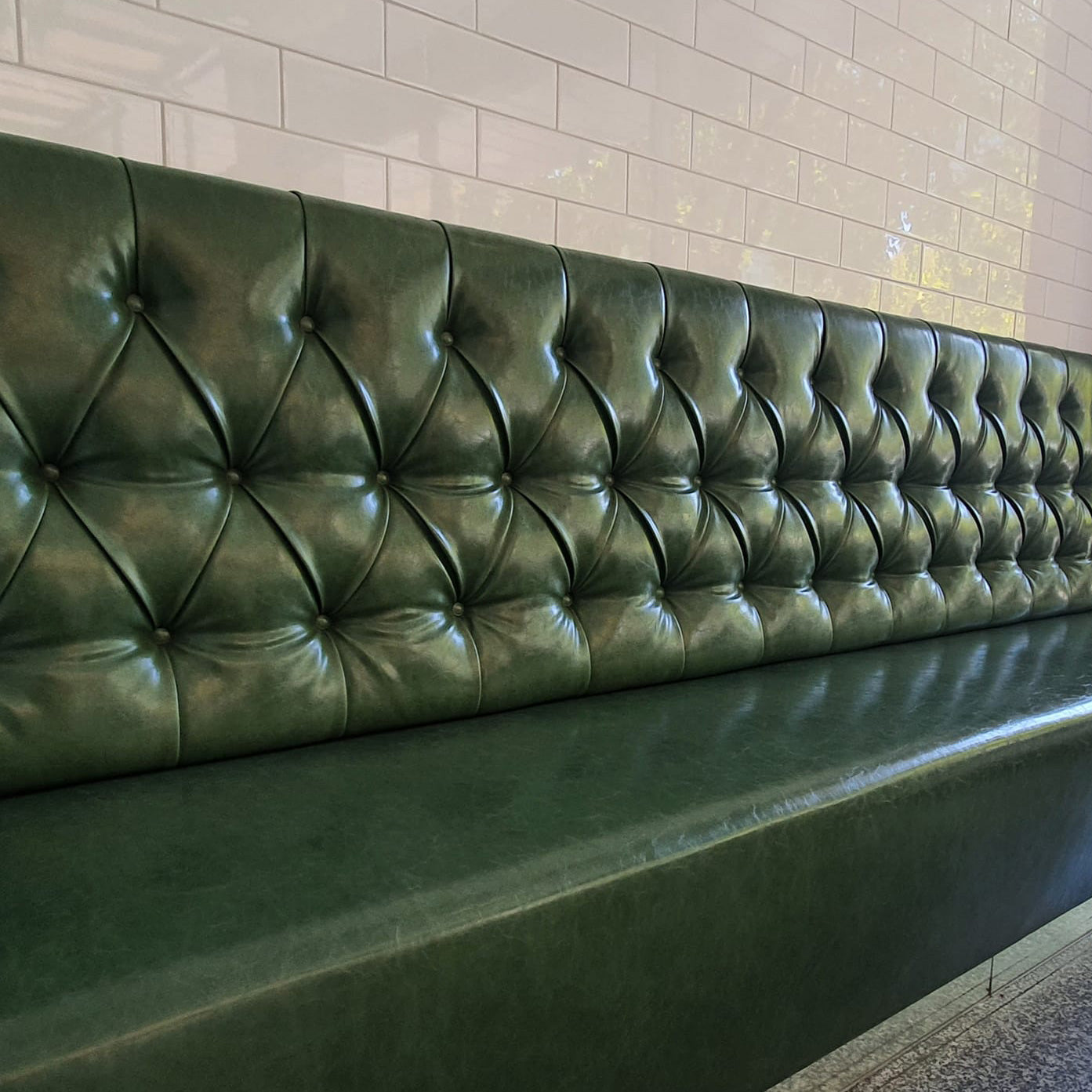 Long green tufted buttons leather bench against a tiled wall.