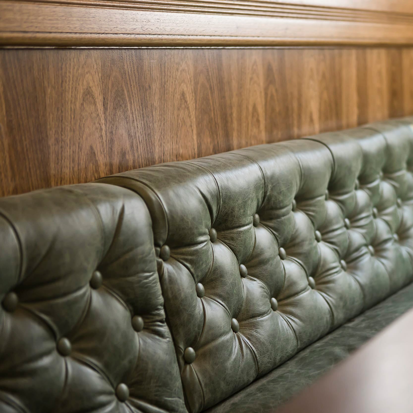 Green leather tufted bench against a wooden paneled wall